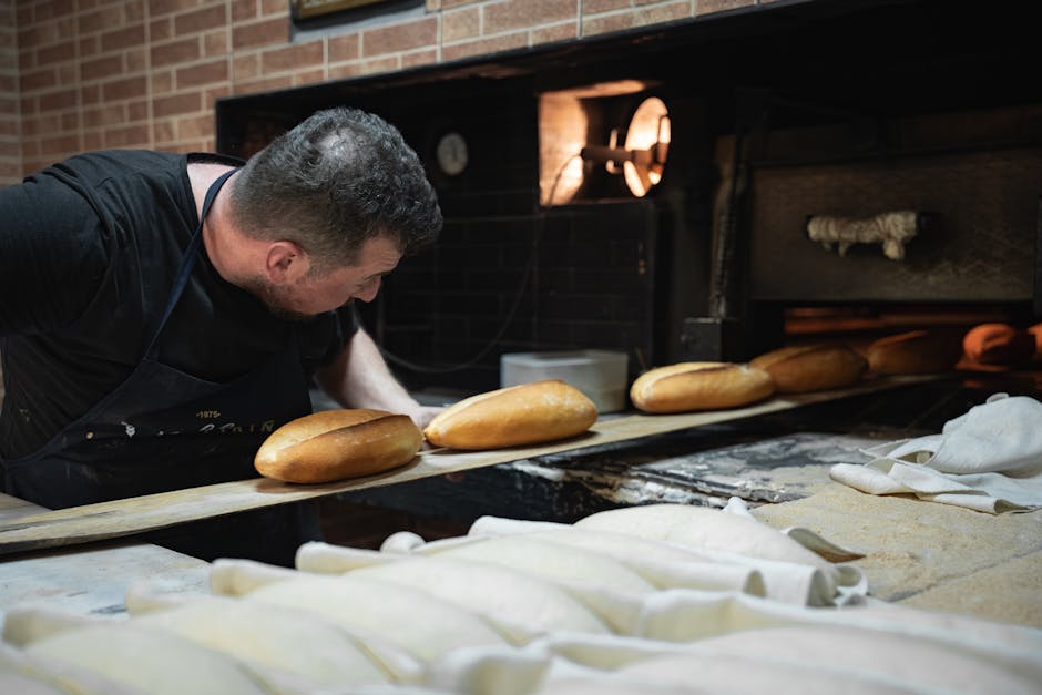 An artisan baker placing loaves of bread in a traditional oven.