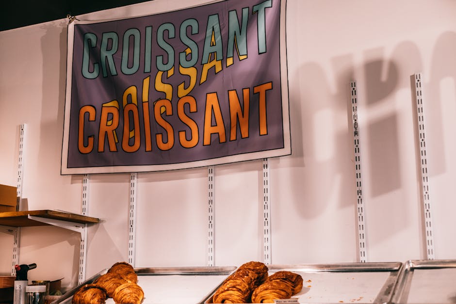 Trays with tasty fresh baked croissants placed near white wall with vivid sign in modern bakery shop with bakery products