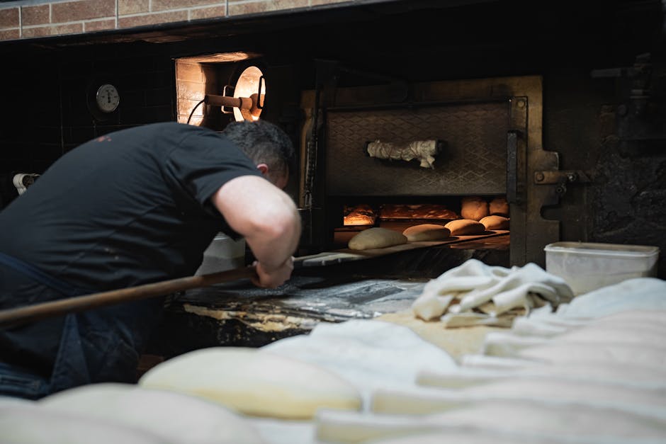 A baker placing loaves in a rustic wood-fired oven, showcasing artisanal bread-making.