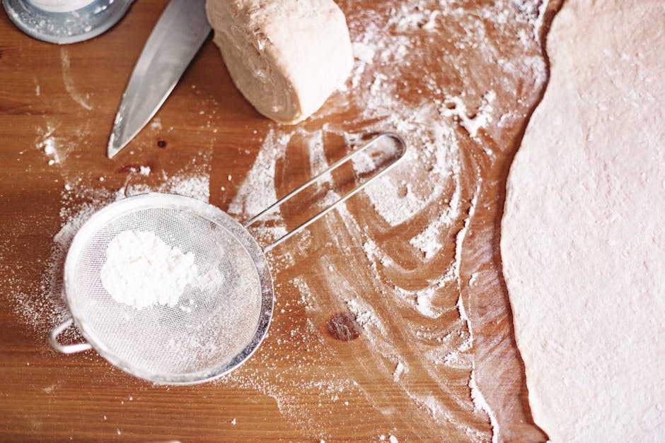 Top view of dough preparation with flour and kitchen tools.